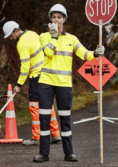 Two individuals in high-visibility workwear, one holding a stop sign. The clothing is bright yellow with reflective stripes.