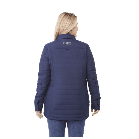 A woman wearing a navy insulated shacket with a logo on the back. The jacket features a quilted design.