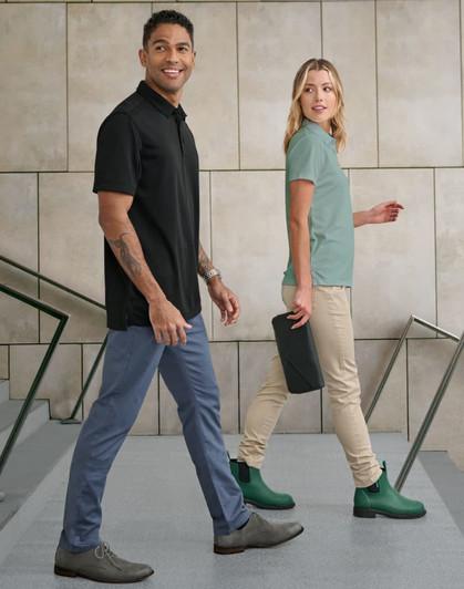 A pair of models walking, wearing black and mint polo shirts, with tan flexi chino pants, and green boots.