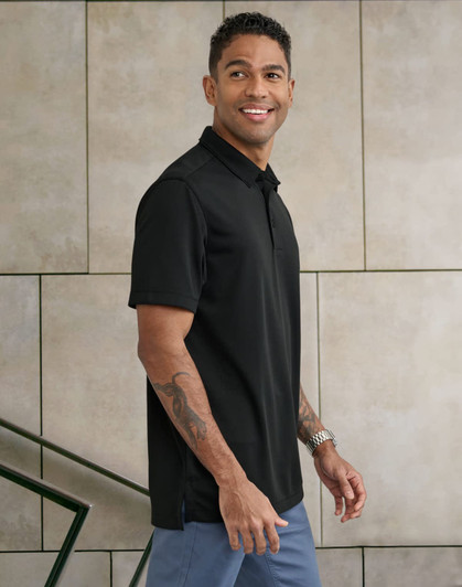 A man wearing a black short-sleeve polo shirt stands against a textured wall, showcasing a sleek design and fit.