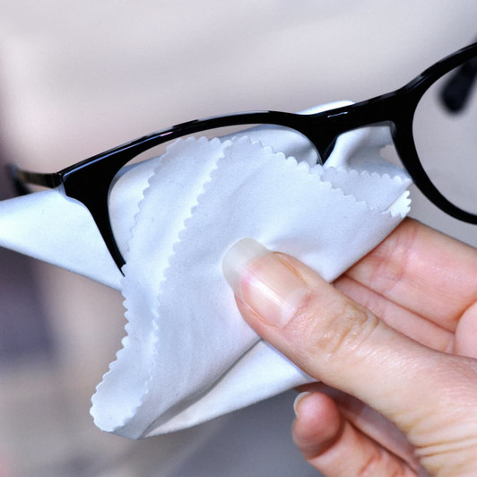 A microfibre cleaning cloth in white being used to clean black glasses. The cloth has a soft texture and rounded edges.