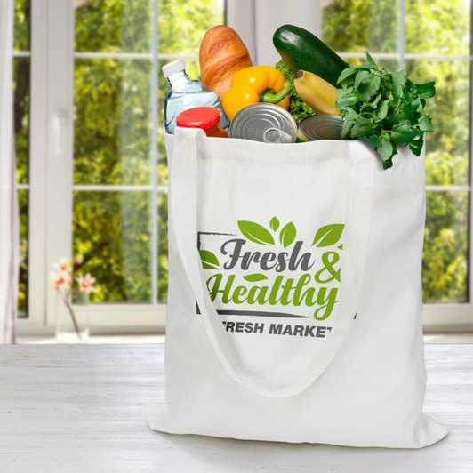 A white bamboo tote bag filled with groceries including vegetables, bread, and water bottles, with a logo on the front.
