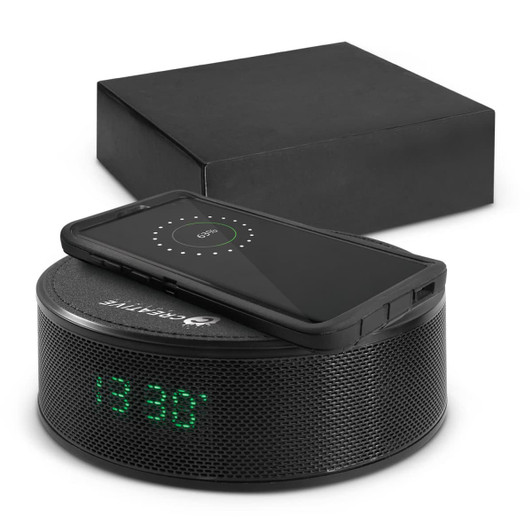 A black wireless charger and speaker with a digital clock display, accompanied by a black box.