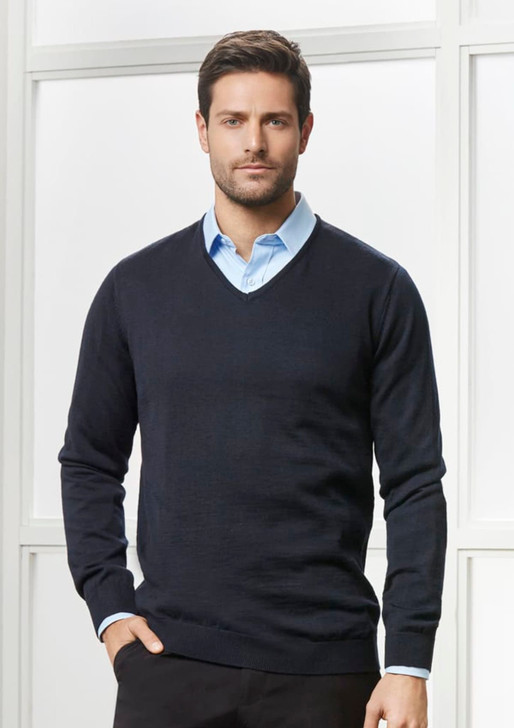 A navy blue pullover sweater with a V-neck, worn over a light blue shirt. The model stands against a bright background.