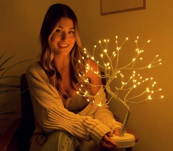 A smiling customer holding a glowing fairy-light tree lamp in her lap