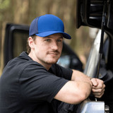 A blue and black cap with a logo, displayed on a person leaning against a vehicle. A blue and black cap with a logo, displayed on a person leaning against a vehicle.