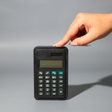 A black calculator with a display and buttons, being held by a hand against a grey background.