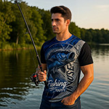 A man wearing a blue and black fishing T-shirt with a fishing design, holding a fishing rod by a lake.