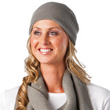 A grey knitted beanie worn by a smiling woman, paired with a textured scarf. The beanie has a simple logo.