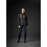 A women's black thermal shell jacket with a quilted design, paired with dark jeans and boots, displayed against a dark background.