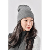 A grey knit beanie worn by a woman with long, dark hair, featuring a simple design and a logo.