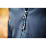 A close-up of a navy blue softshell jacket featuring a zippered front and a logo on the zipper pull.
