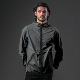 A man wearing a dark grey hooded rain jacket with a zip and a logo on the chest.
