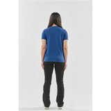 A woman stands with her back to the camera, wearing a blue Settebello Tee and black pants. The shirt has a logo.