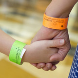 A close-up of two hands holding each other, wearing green and orange Tyvek wristbands.