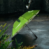 A bright green golf umbrella with a patterned design, featuring a logo on the canopy, set against a textured background.