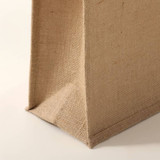 A jute bag in a natural beige colour with a square base and textured surface. It features a simple design.