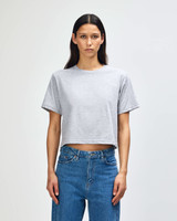 A woman stands wearing a grey boxy T-shirt paired with blue jeans, featuring a logo on the shirt.