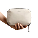 A hand holds a tan Bellroy Lite Tech Kit, featuring a soft-textured exterior and a zip closure.