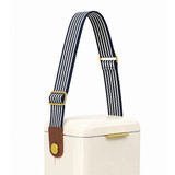 A cooler with a cream body features a navy and white striped shoulder strap and a brown leather accent.