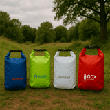 Four dry bags in blue, green, white, and red, featuring logos on each bag, set in a grassy outdoor area. Four dry bags in blue, green, white, and red, featuring logos on each bag, set in a grassy outdoor area.