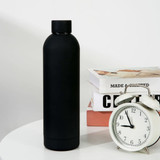 A drink bottle in matte black, positioned next to a vintage alarm clock and decorative books on a table. A drink bottle in matte black, positioned next to a vintage alarm clock and decorative books on a table.