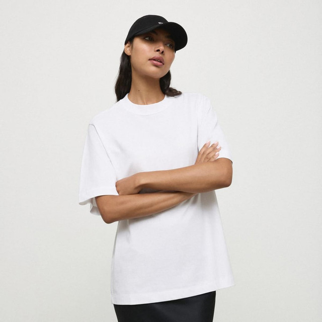 A white essential T-shirt worn by a model, paired with a black cap, showcasing a relaxed fit. A white essential T-shirt worn by a model, paired with a black cap, showcasing a relaxed fit.