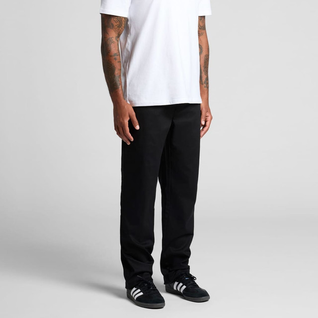 Straight elastic pants in black, worn by a person with tattoos, paired with a white t-shirt and black shoes.