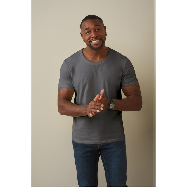 A man wearing a grey crew neck t-shirt and blue jeans, smiling and gesturing with his hands.