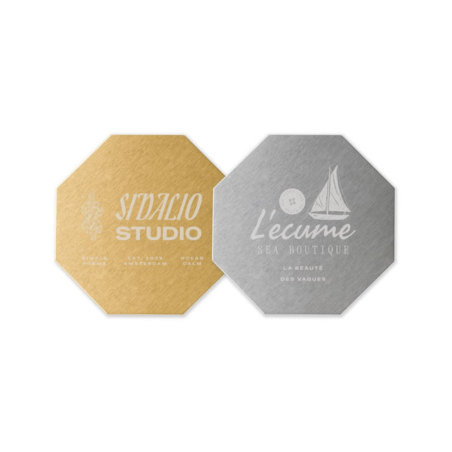 An octagonal metal coaster in gold and silver finishes, featuring logos on each side.