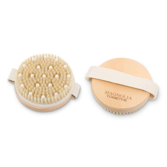 An exfoliating brush with soft massage nodules, featuring a natural wooden base and a fabric strap.