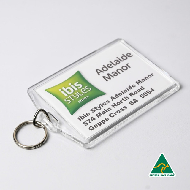 A clear hotel keychain with a ring, featuring green and white branding and a printed address. Australian made.