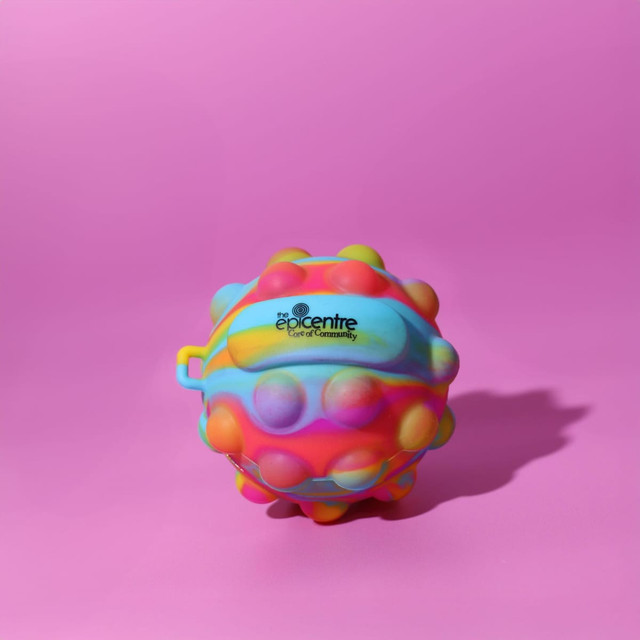 A vibrant, multicoloured stress ball with a textured surface and a logo. It rests on a pink background.