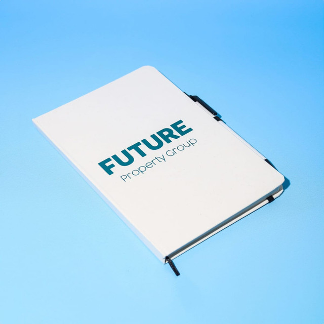 A white A5 notebook with a logo and a black pen resting on a blue background.