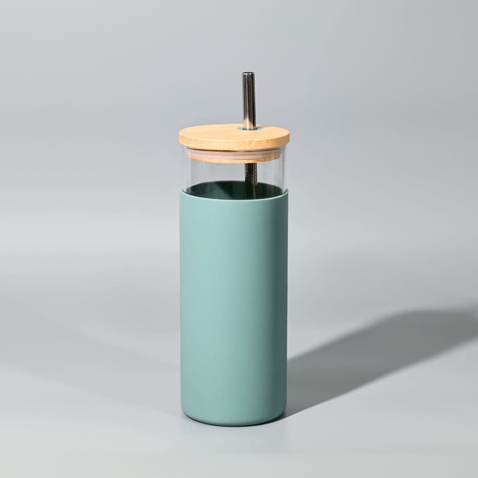 A drink bottle in a mint green silicone sleeve with a clear glass body and wooden lid featuring a straw.