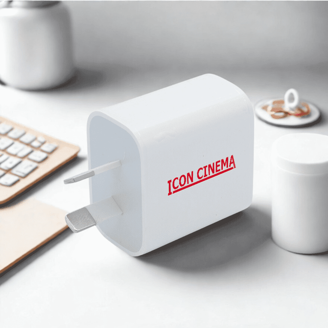 A white travel adapter with a plug and a branding logo, set on a minimalist desk with a keyboard and cup.