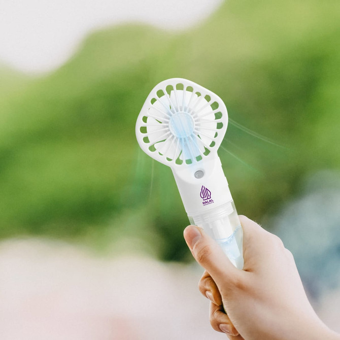 A handheld spray fan in white and light blue, being held against a blurred green background.