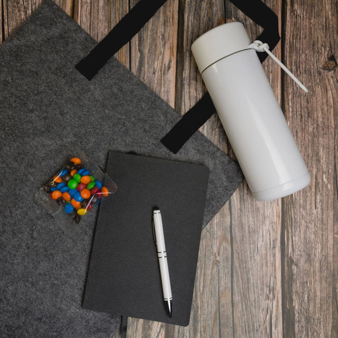 A gray tote bag, a white drink bottle, a black notebook, a silver pen, and a container of colorful candy.