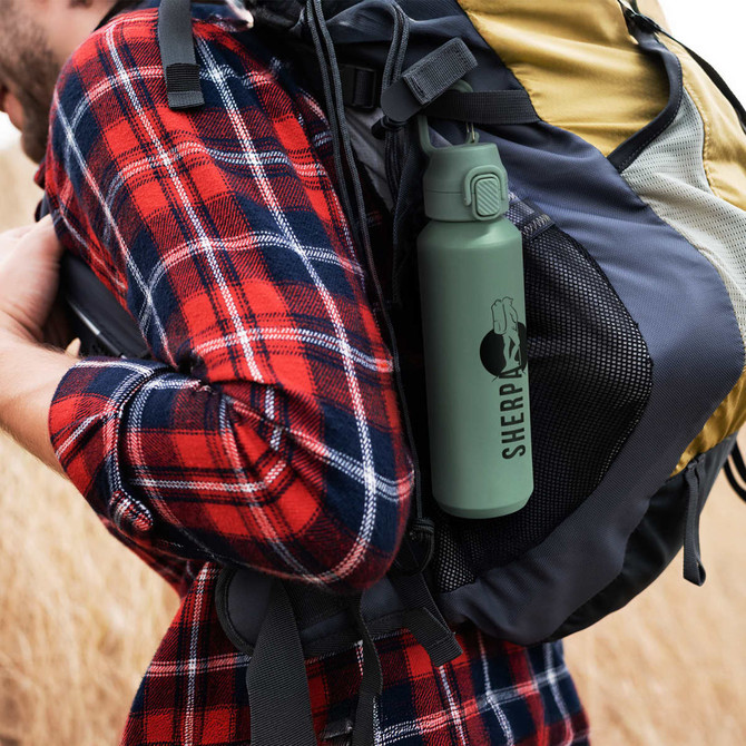 A drink bottle in matte green with a logo, nestled in a mesh pocket of a backpack.
