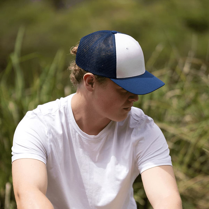 A navy and white trucker cap with a mesh back, worn by a person sitting outdoors in casual clothing.
