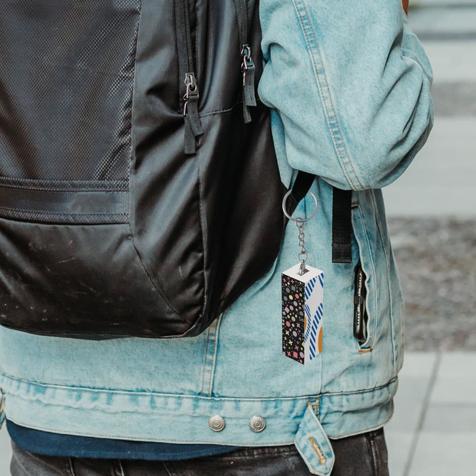 A custom square cube with keyrings attached to a backpack, featuring a colourful design and a logo.