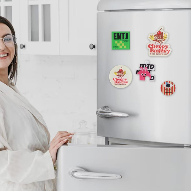 A fridge covered with colourful acrylic magnets depicting various designs, alongside a person interacting with the fridge.