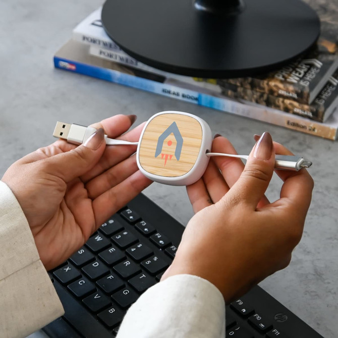 A fast charging cable with a wooden and white design, featuring a logo, held in hands above a keyboard.