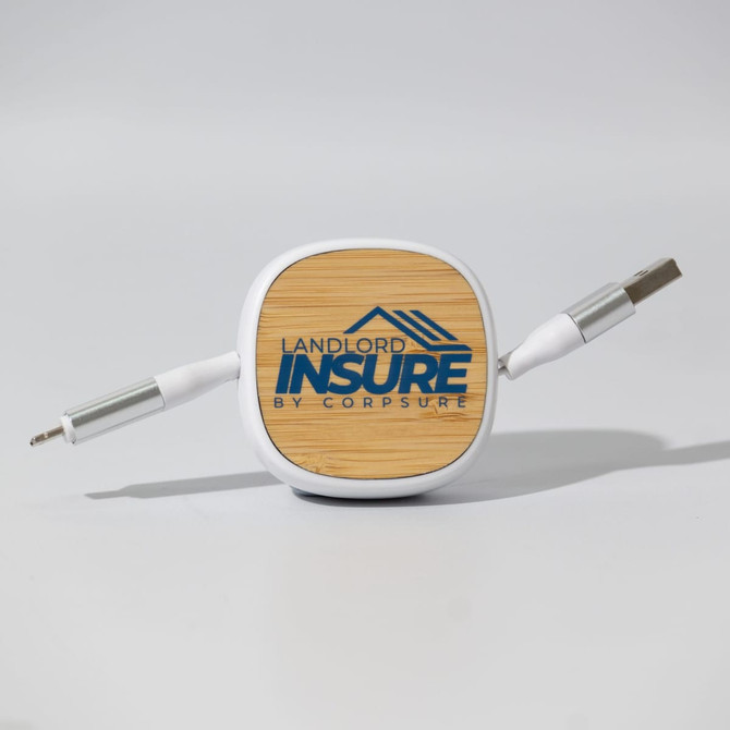 A square cable organiser with a wooden top and two grey charging cables extending from it.