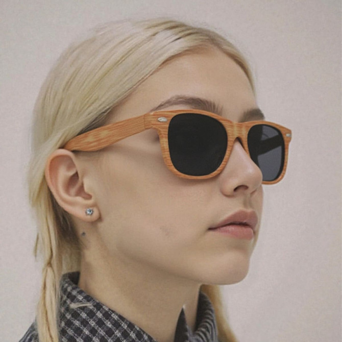 Wooden sunglasses with a light brown frame and dark lenses worn by a person with blonde hair.