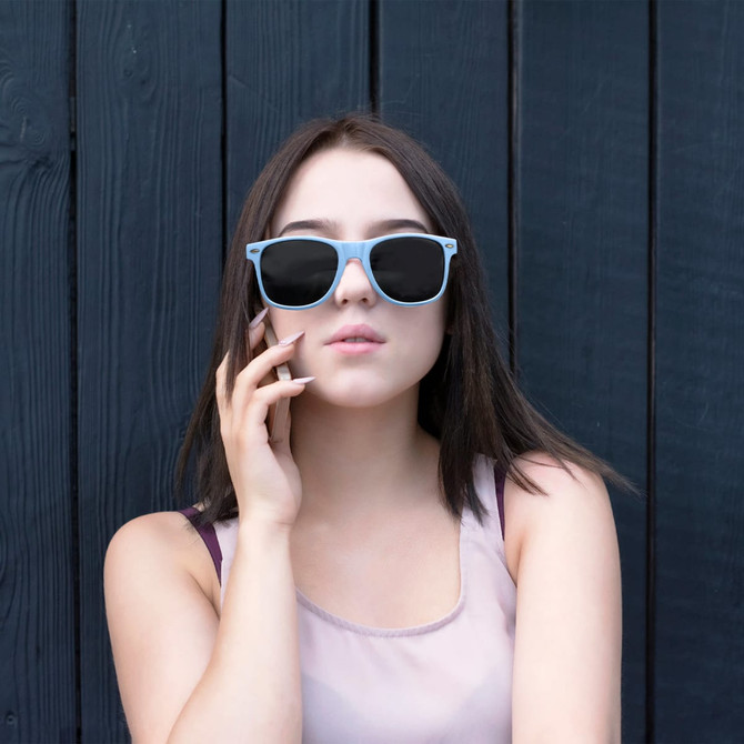 A pair of light blue RPET sunglasses worn by a person with long dark hair against a dark wooden background.