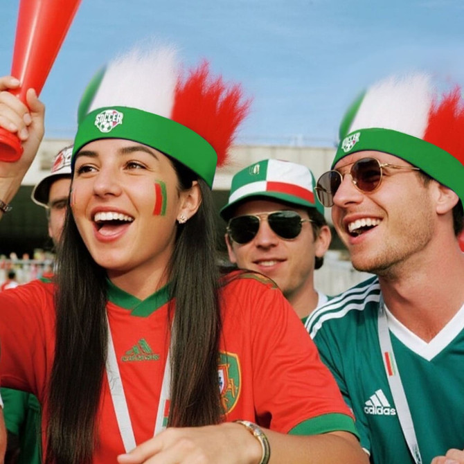 A group of fans wearing green and red headbands with white feathers, showing their support for a sports event.