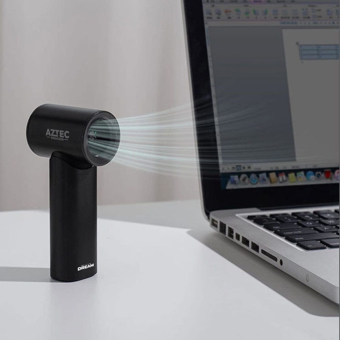 A black handheld fan with a sleek design, positioned next to a laptop on a desk. It features a logo.