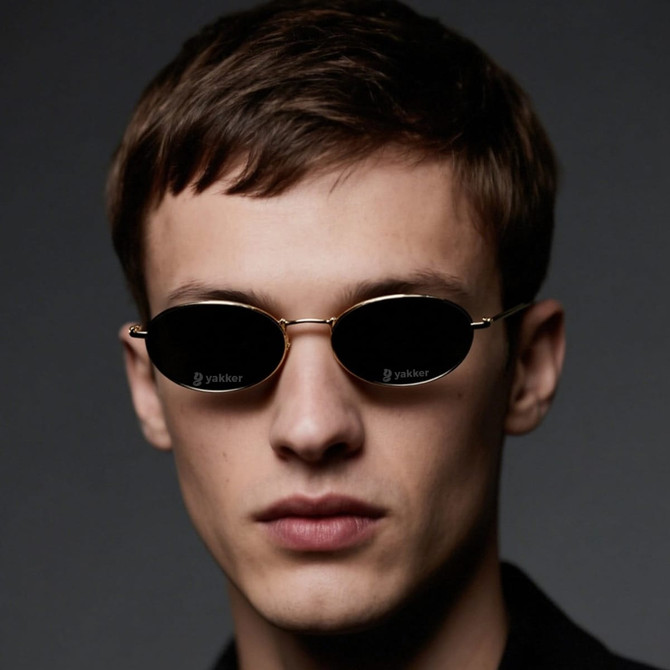 Oval retro sunglasses with a gold frame and dark lenses, worn by a model with short hair against a dark background.