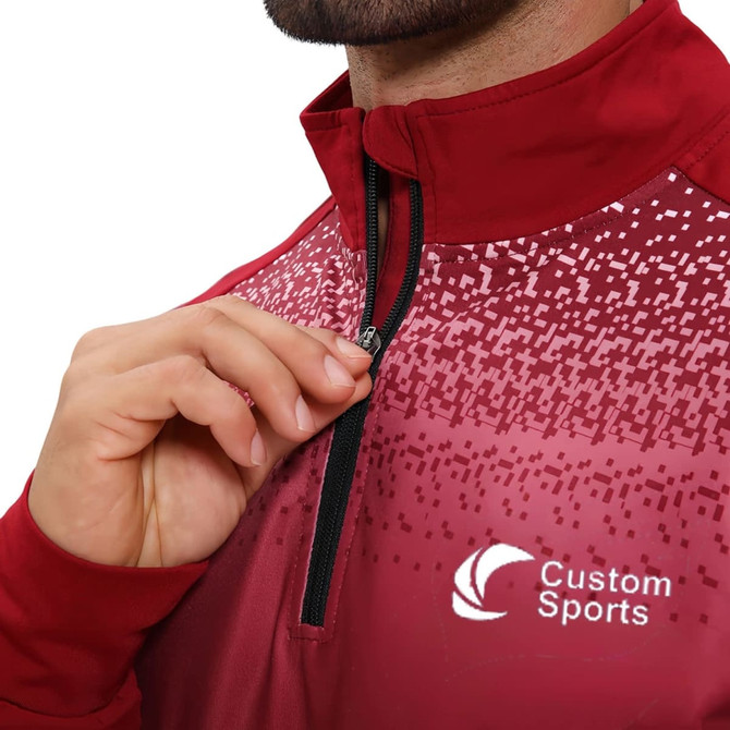 A maroon quarter-zip raglan jacket with a stand-up collar, featuring a logo. The design includes a patterned gradient.